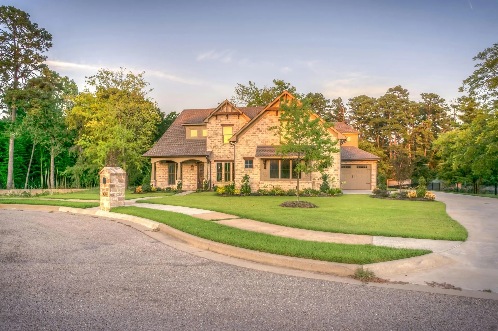Two-story brick house with green lawn, driveway, and trees under a clear sky.