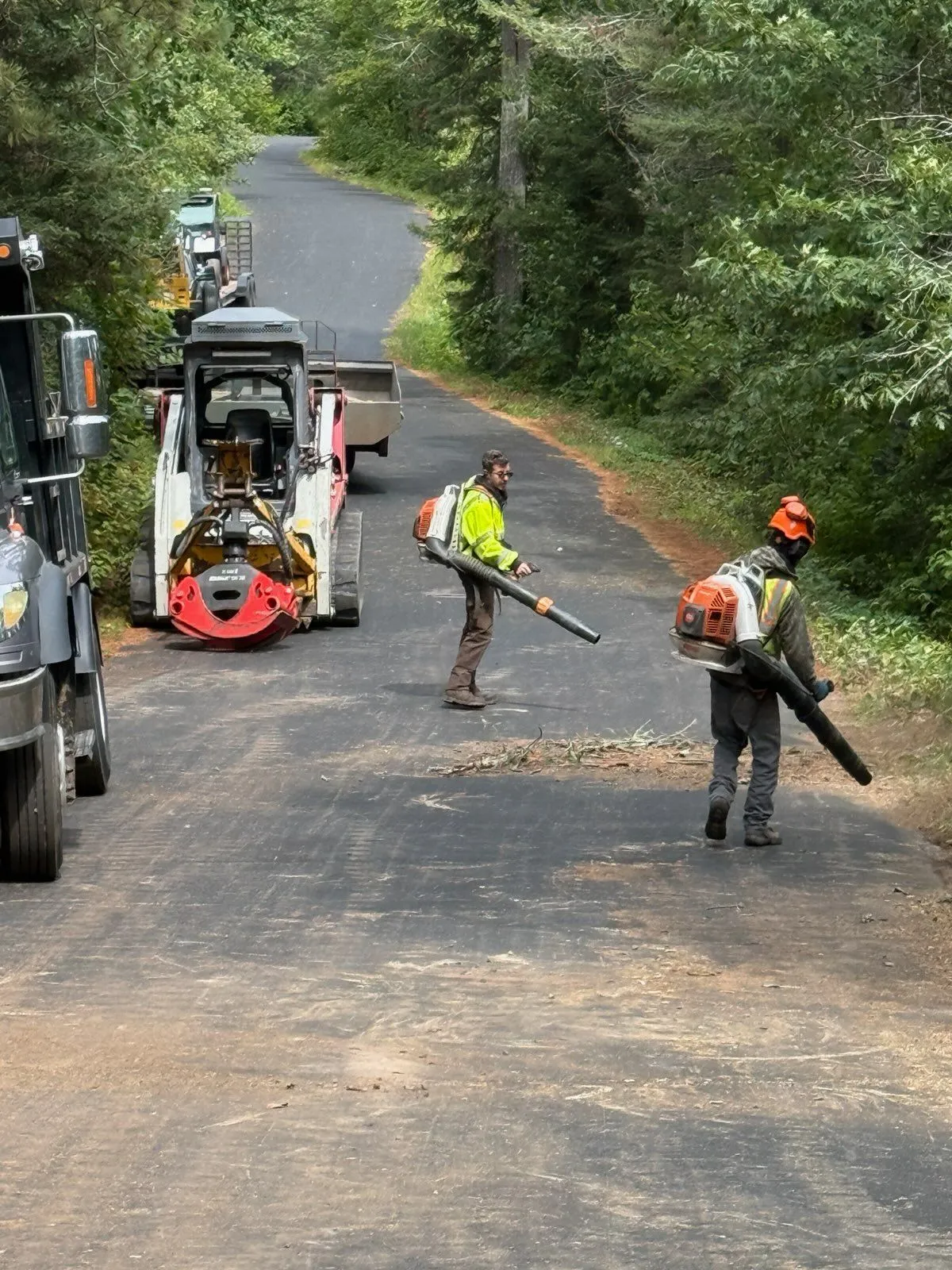 Quality Tree Service crew clearing debris from a rural road with backpack blowers after tree work